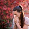 Frau niest vwegen Allergie vor blühendem Busch