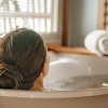 Eine Frau entspannt sich in der Badewanne, nachdem sie erfolgreich gelernt hat, wie man ein Basenbad selber machen kann.