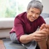 bewegliche ältere Frau sitzt am Boden und hält ihre Füße