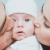 Baby wird von von einem Mann und einer Frau auf jeweils eine Wange geküsst