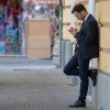 Ein Mann lehnt gedankenverloren an einer Wand und starrt auf sein Handy. 
