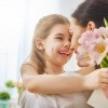 Eine Mädchen überreicht ihrer Mama Blumen und eine Grußkarte