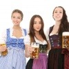 Drei Frauen stehen nebeneinander im Dirndl und halten jeweils einen großen Bierkrug in der Hand