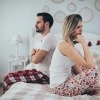 Frau sitzt abgewandt vom Mann auf dem Bett und begeht emotionale Erpressung