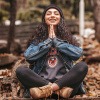 Im Wald in Meditationshaltung sitzende Frau beim Abbauen von Stress