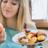 Eine Frau hält einen Apfel und ein Teller mit Süßem und entschließt sich für eine Ernährungsumstellung