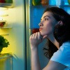 Frau steht beim Kühlschrank und sucht Essen aus Langeweile