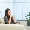Eine Frau sitzt mit Erkältung auf einer Couch