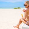 Eine Frau sitzt am Strand und gibt Sonnenschutz auf Ihre Schulter