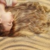 Eine Frau liegt mit ihrer Frisur am Sandstrand im Sommer