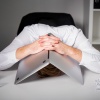 Ein frustrierter Mann versteckt sein Gesicht unter einem Laptop