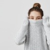 Frau versteckt ihr Gesicht mit Pigmentflecken im Pullover