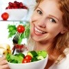 Frau ist Salat und Tomaten als gesunde Ernährung vor einem Kühlschrank
