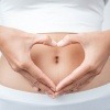 Eine Frau formt mit ihren Händen ein Herz vor dem Bauch