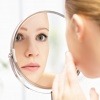 Eine Frau mit glänzender Haut schaut in den Spiegel