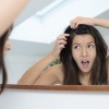 Eine Frau betrachtet im Spiegel ihren Haarausfall