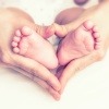 Zwei Hände eines Erwachsenen umfassen zwei Kinderfüße und formen ein Herz