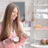 Frau im Badezimmer mit Kokosöl für die Haare in der Hand