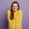 Eine junge Frau mit Brille lacht geschmeichelt und verlegen