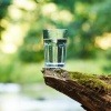 Wasserglas auf einem Stein mit Fluss im Hintergrund.