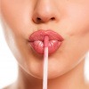 Frau macht einen Kussmund und hält einen Lipgloss an die Lippen