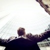 Ein Mann im Anzug steht vor einem modernen Gebäude aus Glas und hebt die Arme in die Luft