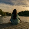 Eine Frau sitzt auf einem Holzsteg am Wasser und meditiert