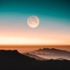 Ein Vollmond ist über Bergen im Sonnenaufgang oder Sonnenuntergang zu sehen