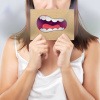 Eine Frau hält sich ein Schild vor den Mund, auf dem ein gezeichneter Mund mit Geruchswolken zu sehen ist.