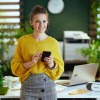 Frau mit Smartphone ist in einem Büro mit Windrad und Wasserflasche als Zeichen für Nachhaltigkeit