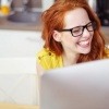 Eine Frau lacht vor einem PC über Online Dating
