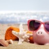 Ein Sparschwein ist auf einem Strand und Utensilien zum Reisen