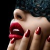Eine Frau mit dunklem Haar trägt einen roten Lippenstift und klassische rot lackierte Fingernägel
