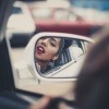 Eine Frau trägt sich im Auto roten Lippenstift auf