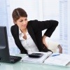 Eine Frau sitzt beim Schreibtisch und hat Rückenschmerzen