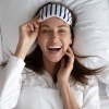 Lachende Frau mit Schlafmaske im Bett wird schön im Schlaf