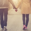 Ein Paar, das Hand in Hand mit jeweils einem Herz in der Hand einen Spaziergang macht