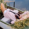 Frau mit Hut liegt im Sommer in einem mit Blumen ausgelegten Boot und lässt sich treiben.