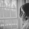 Eine Frau versucht sich im Trauer überwinden, indem Sie vor einem Fenster steht und weint.