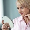 Eine Frau mit trockener Haut im Alter schaut in den Spiegel
