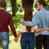 Eine Frau ist verliebt in zwei Männer und geht mit beiden händchenhaltend durch den Park.
