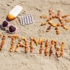 Sonnencreme und Sonnenbrille neben Schriftzug Vitamin D am Strand