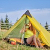 Was braucht man zum Campen? Frau beim Camping im Zelt auf einer offenen Wiese.