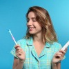 Frau mit schönen Zähnen hält zwei verschiedene Zahnbürsten