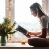 Frau sitzt mit Kerzen am Fensterbrett und liest