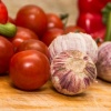 Viele Tomaten liegen neben drei Zehen Knoblauch