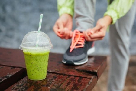 Jemand bindet sich die Schuhe für Sport, davor steht ein Smoothie