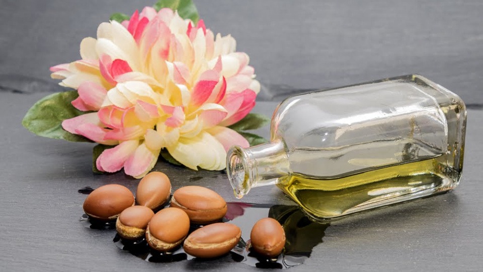 Aus einer Flasche fließt Arganöl, daneben liegen die Früchte Aus einer Flasche fließt Arganöl, daneben liegen Früchte