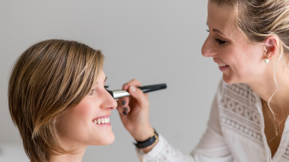 Für eine Braut sollte das Make-up nicht nur toll aussehen, sondern auch lange halten Eine Frau ist dabei, eine Braut mit Make-up zu schminken