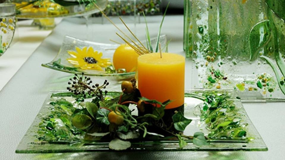 Besonders Blumen und Kerzen passen zur Glasdekoration. Gelbe Kerze auf Glasteller.